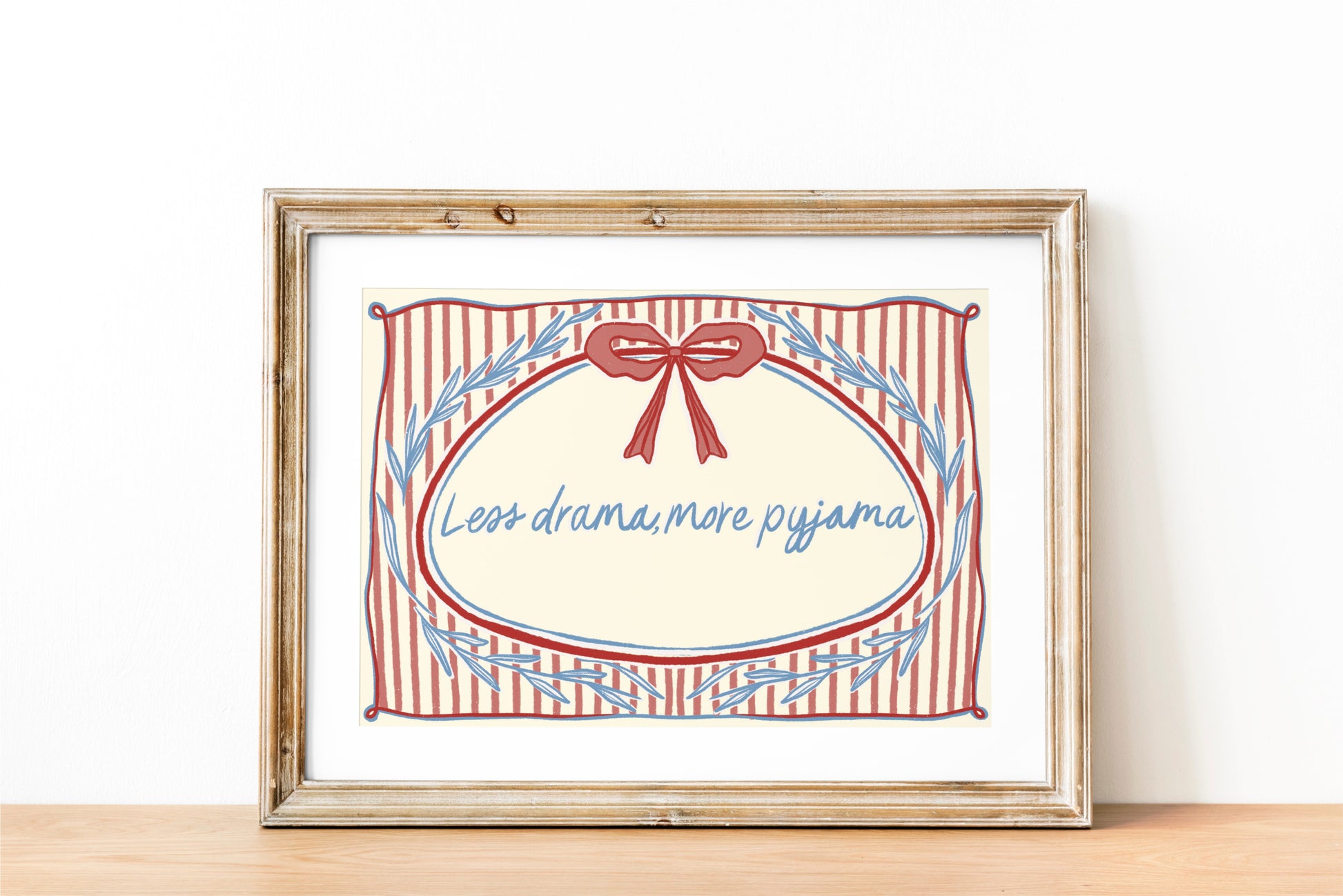 landscape orientation print with a beige background, pink stripes and a pink bow with red outline in the top middle. blue outlines of leave form an oval in the center and the quote reads in blue hand writing "less drama more pyjama"