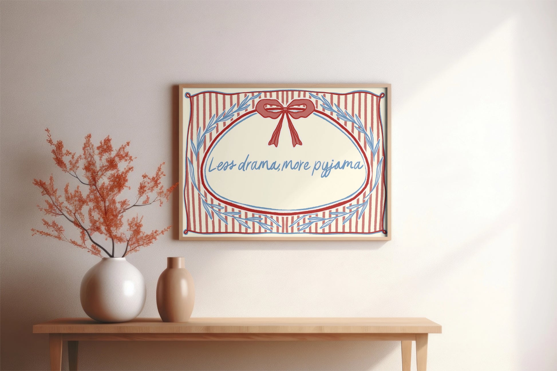 landscape orientation print with a beige background, pink stripes and a pink bow with red outline in the top middle. blue outlines of leave form an oval in the center and the quote reads in blue hand writing "less drama more pyjama"