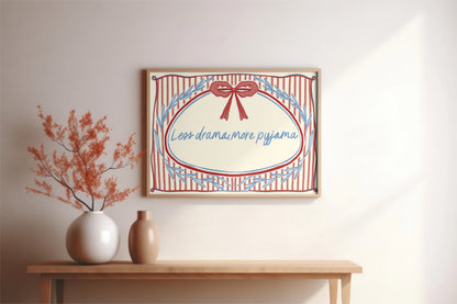 landscape orientation print with a beige background, pink stripes and a pink bow with red outline in the top middle. blue outlines of leave form an oval in the center and the quote reads in blue hand writing "less drama more pyjama"