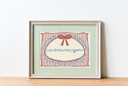 landscape orientation print with a beige background, pink stripes and a pink bow with red outline in the top middle. blue outlines of leave form an oval in the center and the quote reads in blue hand writing "less drama more pyjama"