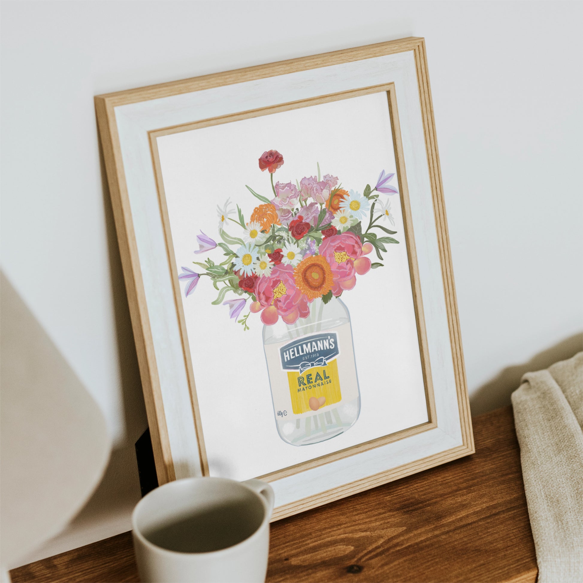 Framed artwork of a colourful bouquet of flowers in an empty Hellmann's mayonnaise jar on a wooden surface.
